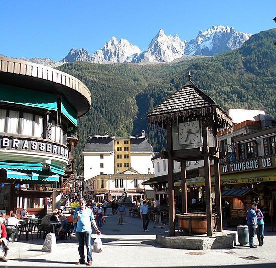 A busy shopping center in the foreground with beautiful snowy mountaintops in the distance of Chamonix, France