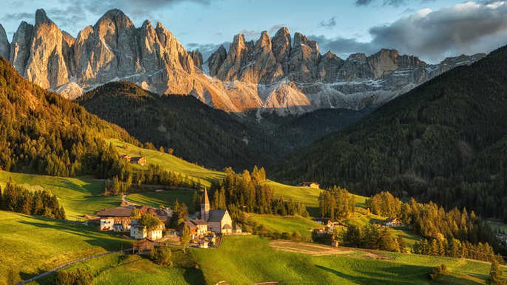 The Dolomite mountains tower over a small village in a valley during sunset.