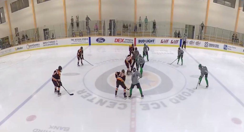 A wide angle shot of two youth hockey teams lined up for a center ice face-off.