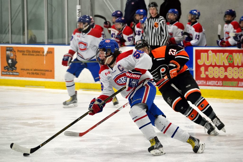 A Junior Canadiens hockey player carries the puck up the ice while a Don Mills Flyers defender chases after him.