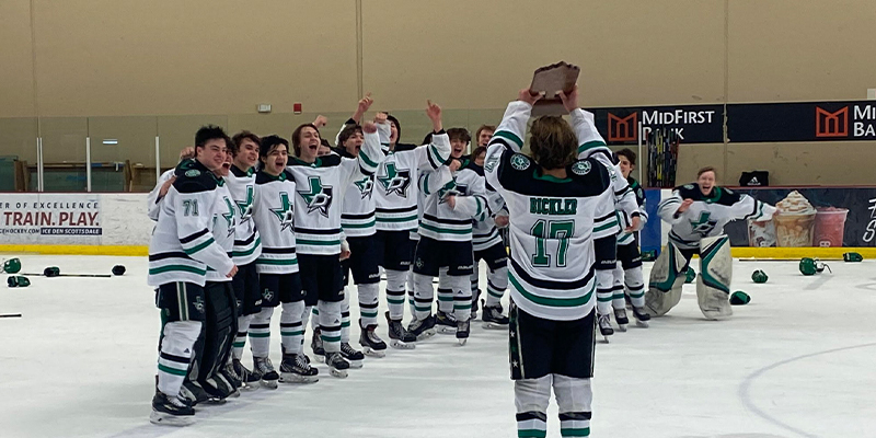 Damon Bickler lifts championship trophy over his head while the rest of the Dallas Stars Elite team cheers.