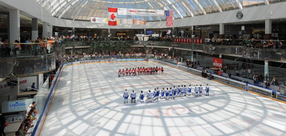 Two hockey teams stand at the blue lines of an ice rink inside the West Edmonton Mall.