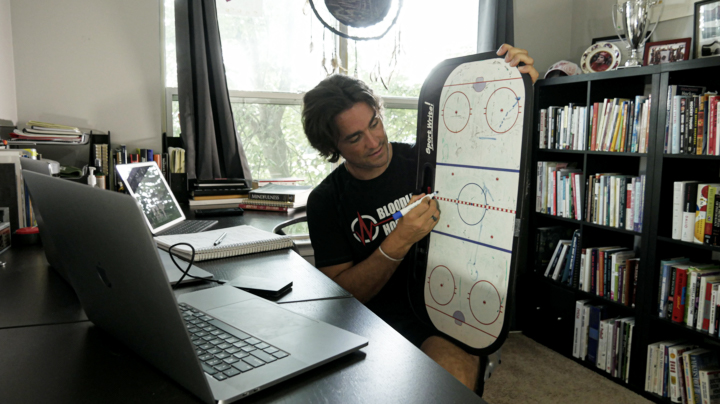 Vince Malts, owner of Bloodline Hockey, sits at his desk while drawing up a play on a white board.