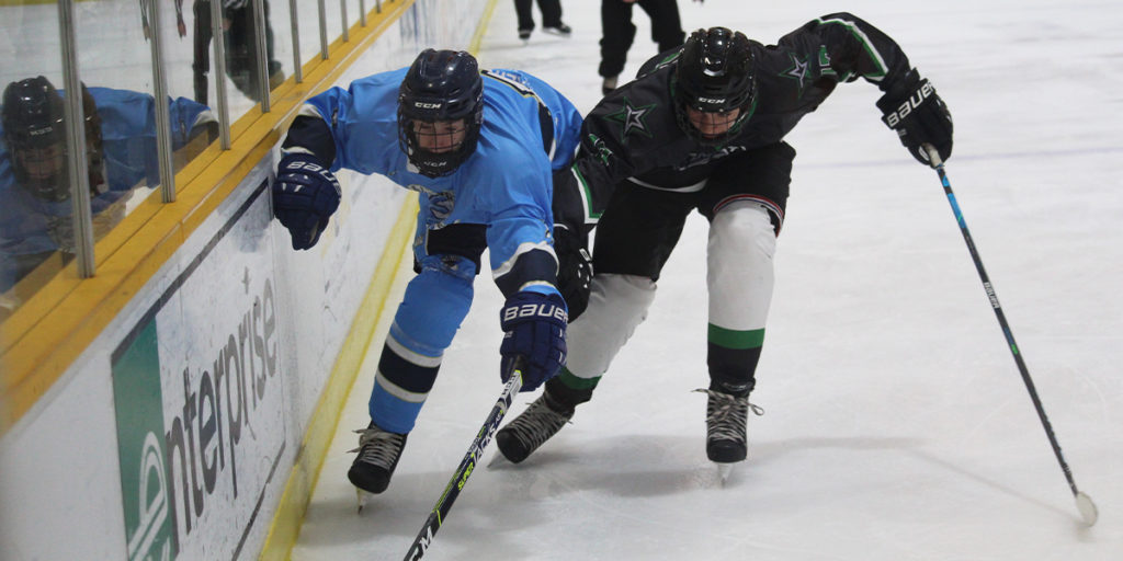 Two players at the 2021 World Selects Trophy race for a loose puck along the boards.